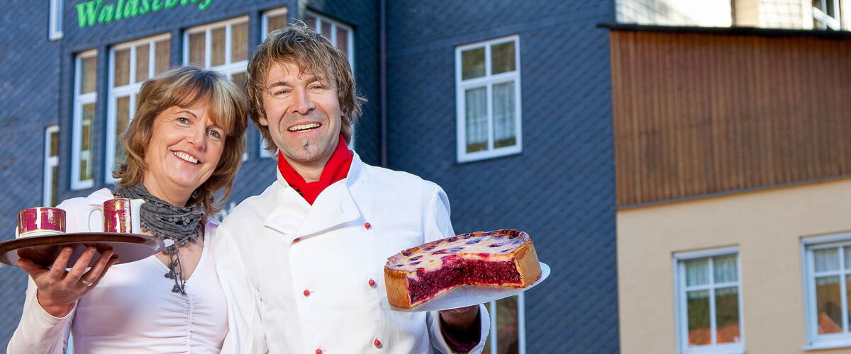 Silke Kühmel und ihr Mann zeigen frisch gebackenen Kuchen und Kaffee vor dem Waldschlösschen in Friedrichroda im Thüringer Wald